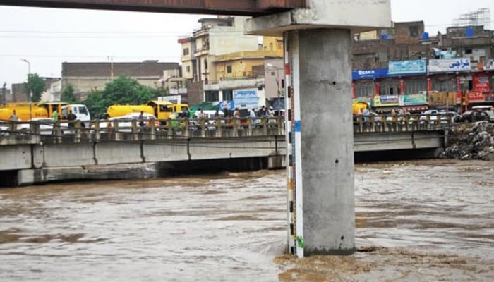 People stand on a bridge at Gawalmandi as water level in Leh Nullah rises to dangerous level. — INP/file