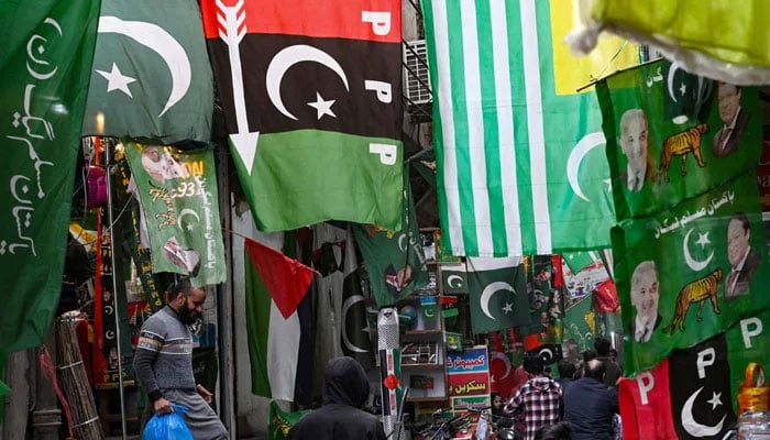 People walk past flags of political parties displayed for sale at a market in Lahore on January 13, 2024. — AFP