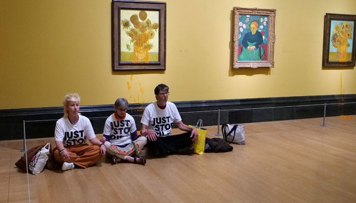 A handout picture from the Just Stop Oil climate campaign group shows three activists sitting on the floor under Vincent van Gogh´s Sunflowers after throwing tomato soup over two paintings at the National Gallery in central London on September 27, 2024. — AFP