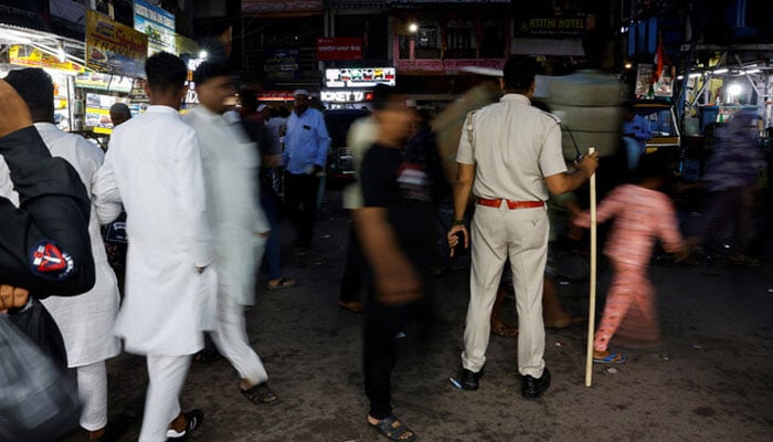 People walk past a policeman standing guard on a busy road in Ajmer, Rajasthan, India, on August 24, 2024. — Reuters