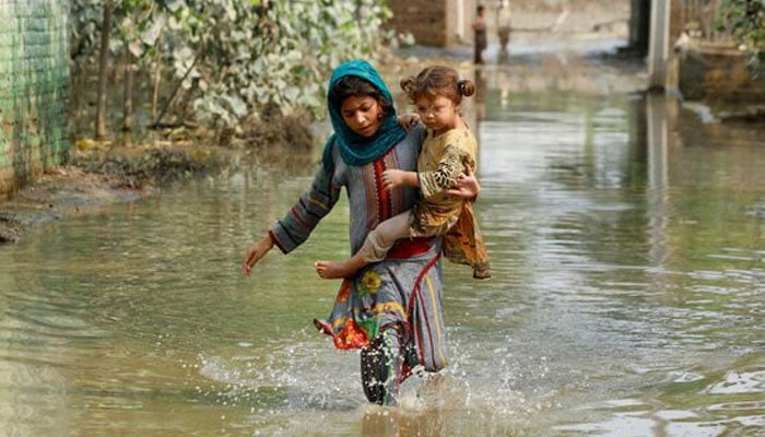 A girl carries a child as she walks through stranded flood water, following rains and floods during the monsoon season in Nowshera on September 4, 2022. — Reuters