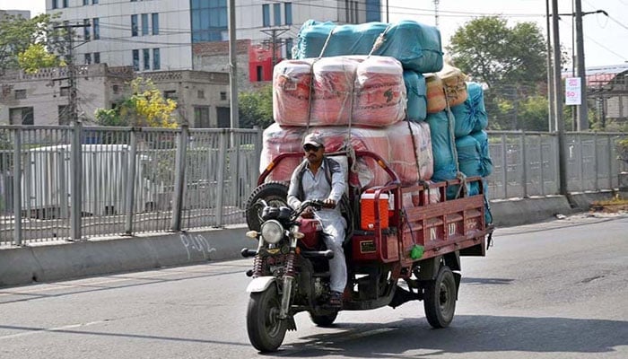 A loader rickshaw driver on his way loaded with a water cooler at Ferozepur Road to deliver to a local market on May 29, 2024. — APP