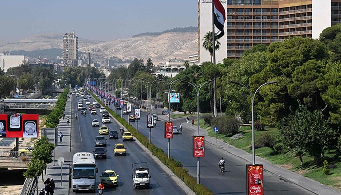 Syrians drive past the Syrian flag at half-mast in the capital Damascus on September 29, 2024, after Syria officially declared a three-day national mourning period following Israels killing of Lebanons Hizbollah leader Hassan Nasrallah. — AFP