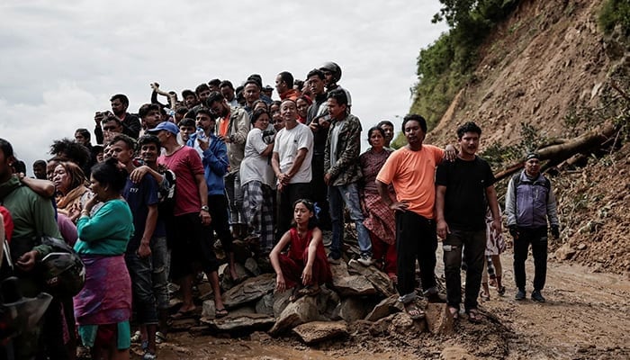 People stranded at the Tribhuwan Highway look on as rescue personnel work to retrieve the bodies of the victims from a landslide triggered by heavy rainfall in Dhading, Nepal on September 29, 2024. — Reuters