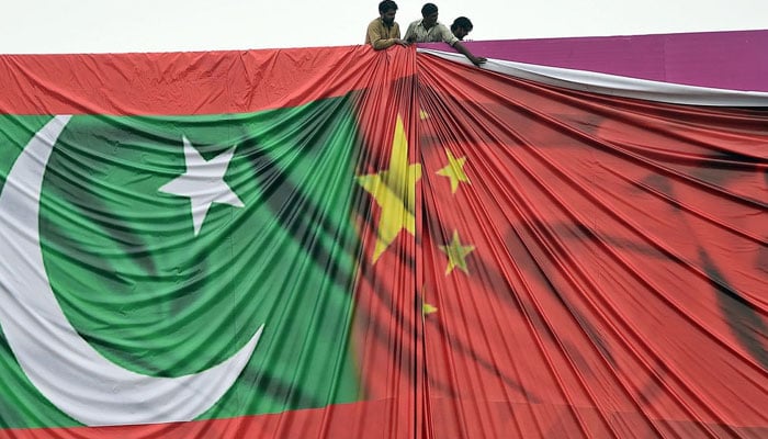 A representational image showing workers adjusting an illustration of national and Chinese flags on a billboard. — AFP/File