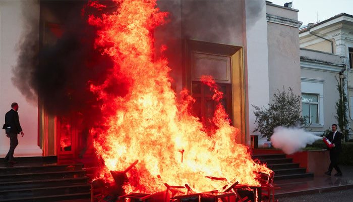 An opposition member of parliament walks near the burning chairs outside the parliament building, as a member of National Guard uses fire extinguisher as members of the opposition burn chairs to protest against the government and the imprisonment of their colleague Ervin Salianji, in Tirana, Albania, September 30, 2024. — Reuters