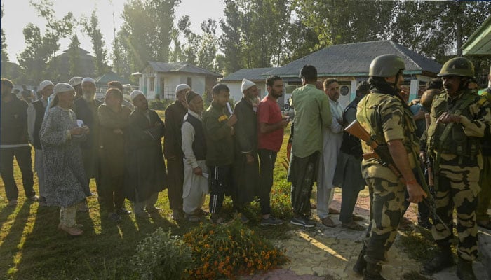 Indian security personnel stand guard as voters queue up to cast their ballots at a polling station during the third and final phase of voting for local assembly elections, in Bandipora. — AFP/file