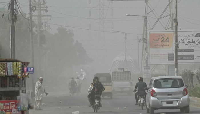 Commuters drive along a road amid a dust storm in Karachi on October 10, 2024. — AFP