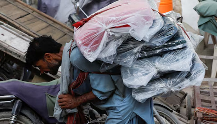 A labourer bends over as he carries packs of textile fabric on his back to deliver to a nearby shop in a market in Karachi on June 24, 2022. — Reuters