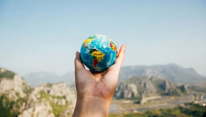 The representational image shows a person holding a world globe facing the mountain.— Pexels/File