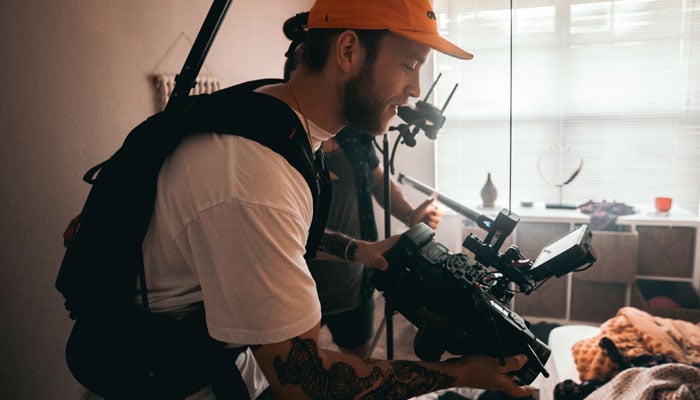 The representational image shows a man handling a video camera while shooting an event. — Unsplash/File