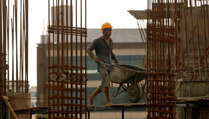 A worker pushes a wheelbarrow to collect cement at a construction site.— Reuters/File