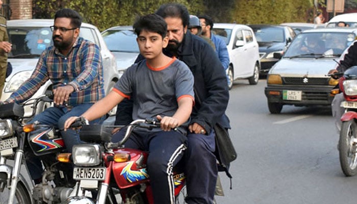 This representational image shows a young boy riding a motorcycle with his father seated with him on the way to a road in Lahore on November 19, 2023. —  Online