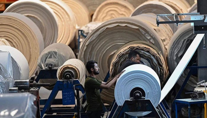 In this picture taken on July 20, 2023, a worker operates a machine preparing fabric at a textile mill in Lahore. — AFP