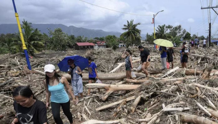 People walk through logs swept away by Tropical Storm Trami in Laurel, Batangas province, south of Manila. —AFP/File