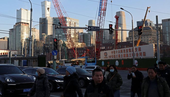 People cross an intersection near cranes standing at a construction site in Beijing, China on January 15, 2024. — Reuters