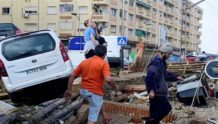 Residents walk next to piled up cars following deadly floods in Sedavi, south of Valencia, eastern Spain, on October 30, 2024. — AFP