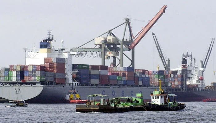 Vessels pass by a container ship being loaded with cargo packed with exports at the Karachi port. — AFP/File