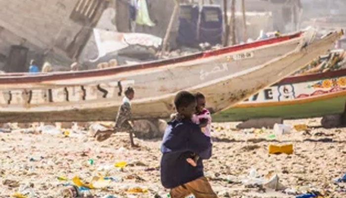 A boy carrying a child walks through an area full of trash. — worldbank.org/File