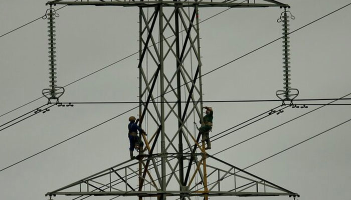 This representational image shows workers working on an electricity pylon. — Reuters/File