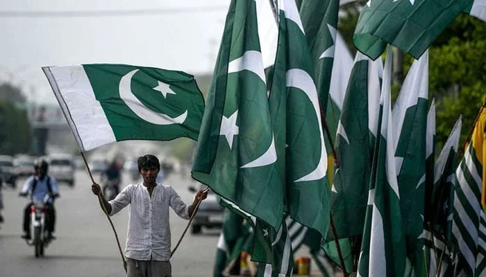 A vendor holds national flags as he waits for customers beside his stall alongside a street in Islamabad. — AFP/File