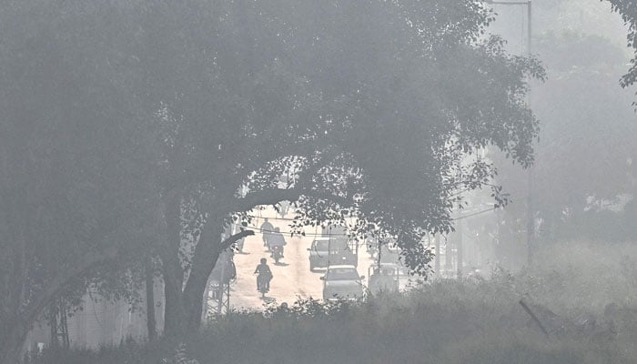 Commuters ride along a road amid smoggy conditions in Lahore on November 4, 2024. — AFP