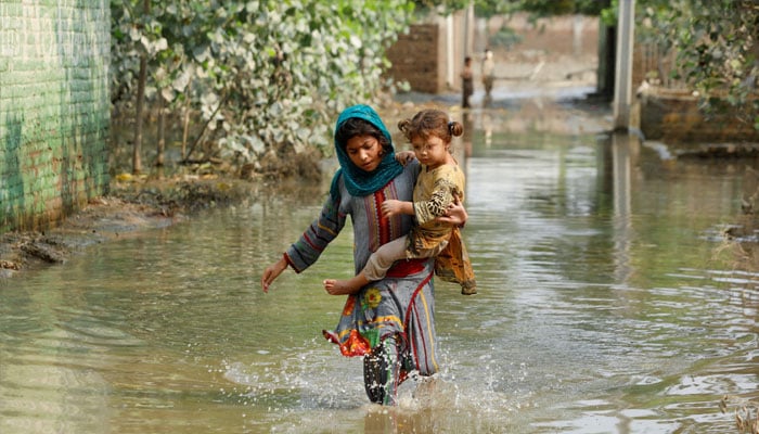 A girl carries her sibling as she walks through stranded flood water, following rains and floods during the monsoon season in Nowshera, Pakistan September 4, 2022. — Reuters