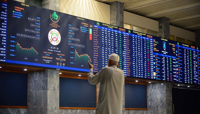 A broker talks on phone as he looks at an index board showing the latest share prices at the PSX in Karachi on February 10, 2023. — AFP