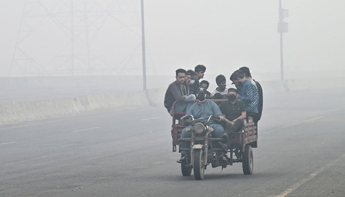 Commuters ride along a road engulfed in smog in Lahore on November 8, 2024. — AFP