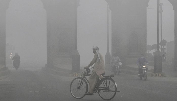 A cyclist rides along a street engulfed in thick smog, in Lahore on November 10, 2024. — AFP