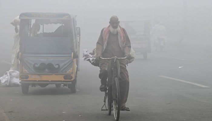 A cyclist rides along a road engulfed in thick smog in Lahore on November 11, 2024. — AFP