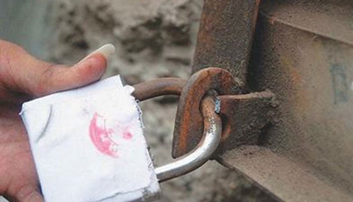 A representational image showing a person holding a padlock placed on a sealed business. — AFP/File