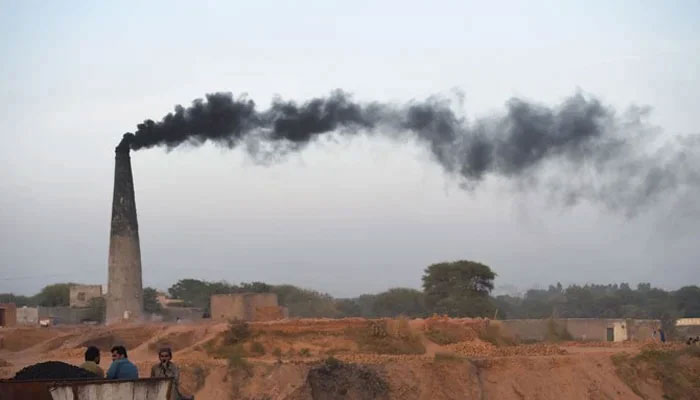 The representational image shows smoke billowing from a brick kiln chimney as labourers are seen taking rest nearby. — AFP/File