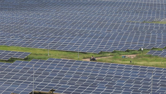 A man rides a motorcycle along the solar panels in Gujarat Solar Park also called Charanka Solar Park at Patan district in Gujarat, India on September 12, 2024. — Reuters