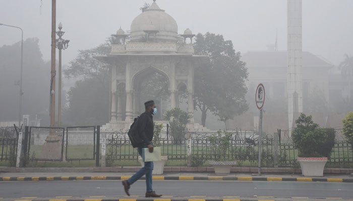 A man wears facemask on the way along a road engulfed in smog in Lahore on November 14, 2024. — Online