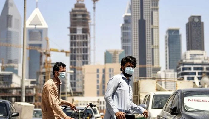 Foreign workers clad in mask walk pushing bicycles along a street in the Satwa district of Dubai on May 6, 2020. — AFP