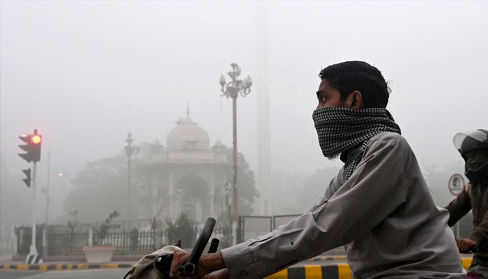 Commuters ride along a street engulfed in smog in Lahore on November 14, 2024. — AFP