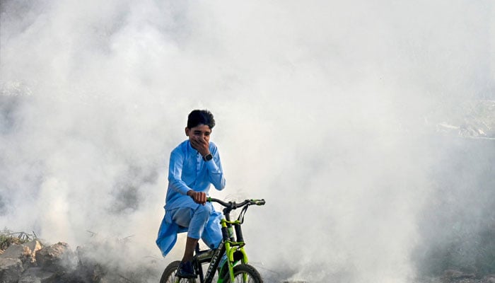 A boy rides past as smoke billows from a burning garbage dump, in Lahore on November 1, 2024.— AFP