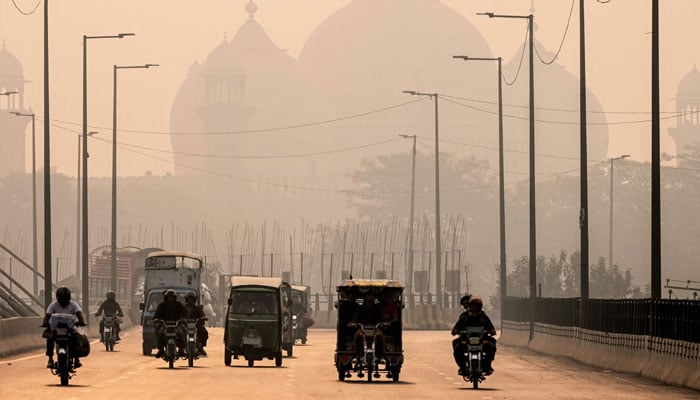 Commuters ride along a street engulfed in smog, in Lahore on November 5, 2024.— AFP