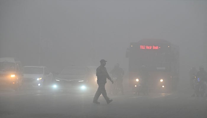 A man crosses a street engulfed in smog in Lahore on November 16, 2024.— AFP