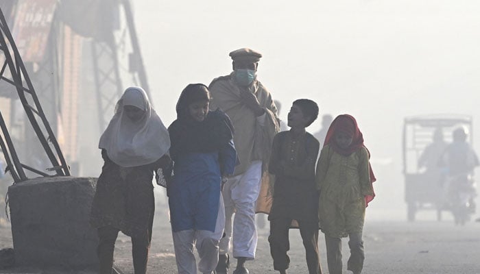 A man wearing a mask walks with children along a street engulfed in smog, in Lahore on November 18, 2024. — AFP