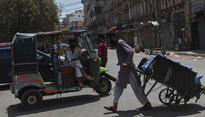 An auto-rickshaw driver wearing a facemask waits for customers on a street in Karachi. — AFP/File