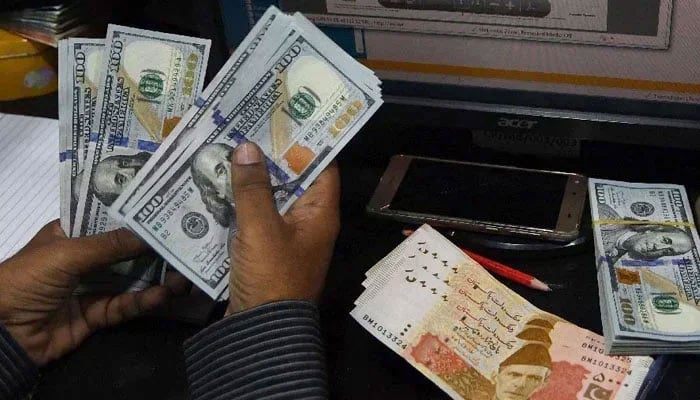 A currency dealer can be seen counting $100 notes while Rs5,000 notes are placed on the table. — AFP/File