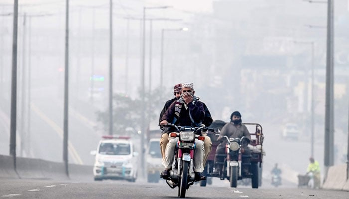 A commuter riding a motorbike covers his face with cloth amid thick smog, along a street in Lahore on November 20, 2024. — AFP