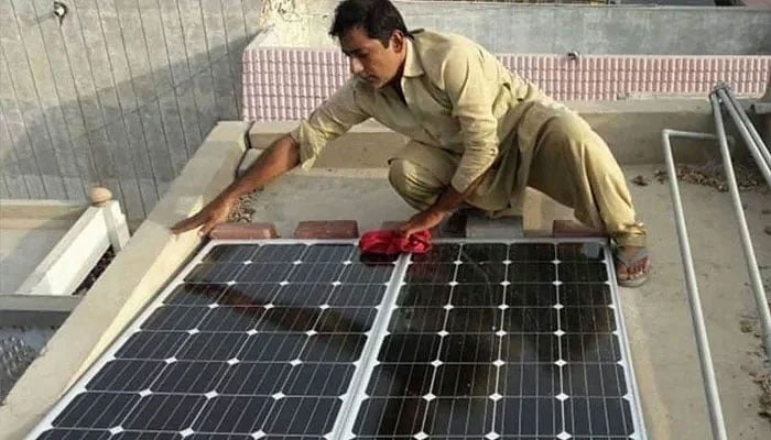 A man wipes the dust off solar panels he recently installed on the roof of his home in Larkana, Sindh. — Reuters/File