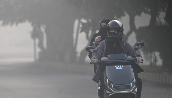 Women ride a motorcycle amid dense smog in Lahore on November 22, 2024. — AFP