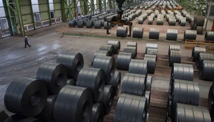 A worker walks by steel rolls at a steel plant in Changshou, Chongqing, China, on August 6, 2018. —Reuters