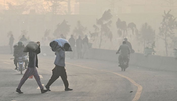 Pedestrians walk along a street amid heavy smog in Lahore on November 25, 2024. — AFP