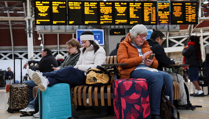 Rail passengers wait with their luggage following train cancellations caused due to Storm Bert on a screen at Paddington Station in London on November 25, 2024. — Reuters