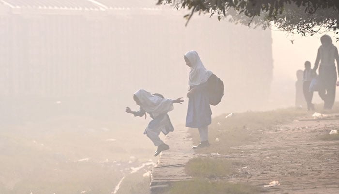 School girls cross a railway track engulfed in smog in Lahore on November 27, 2024. — AFP